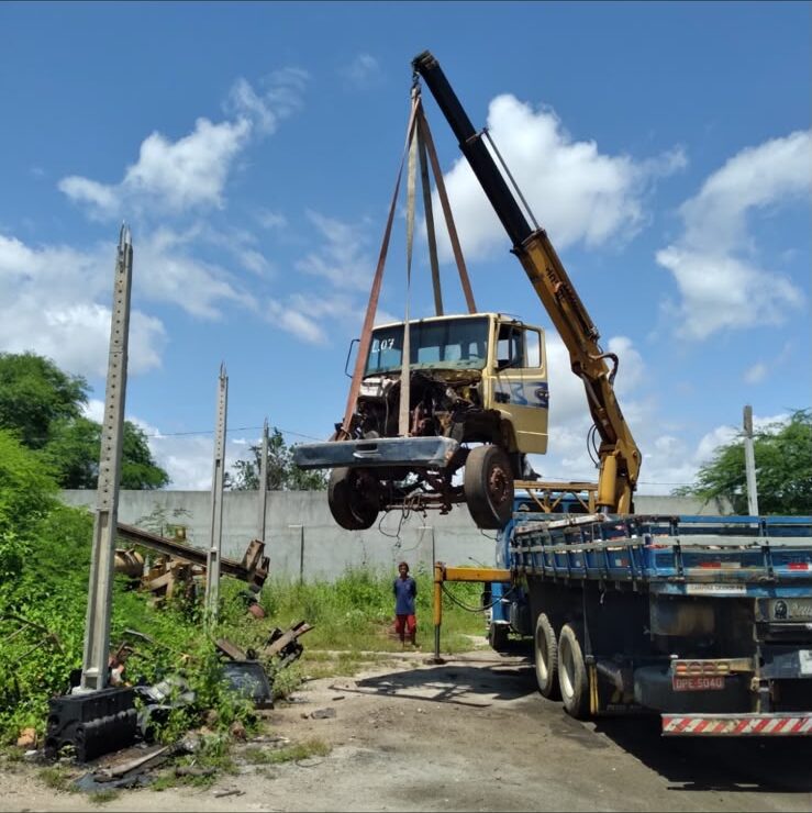 Caminhão munck movimentando equipamento pesado suspenso por cintas